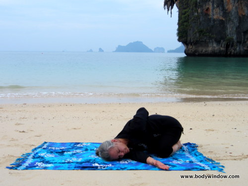 Photo of Elle Bieling doing Wide-Knee Child's Pose with a Twist in Yin Yoga, on Pranang Beach, Railay, Thailand